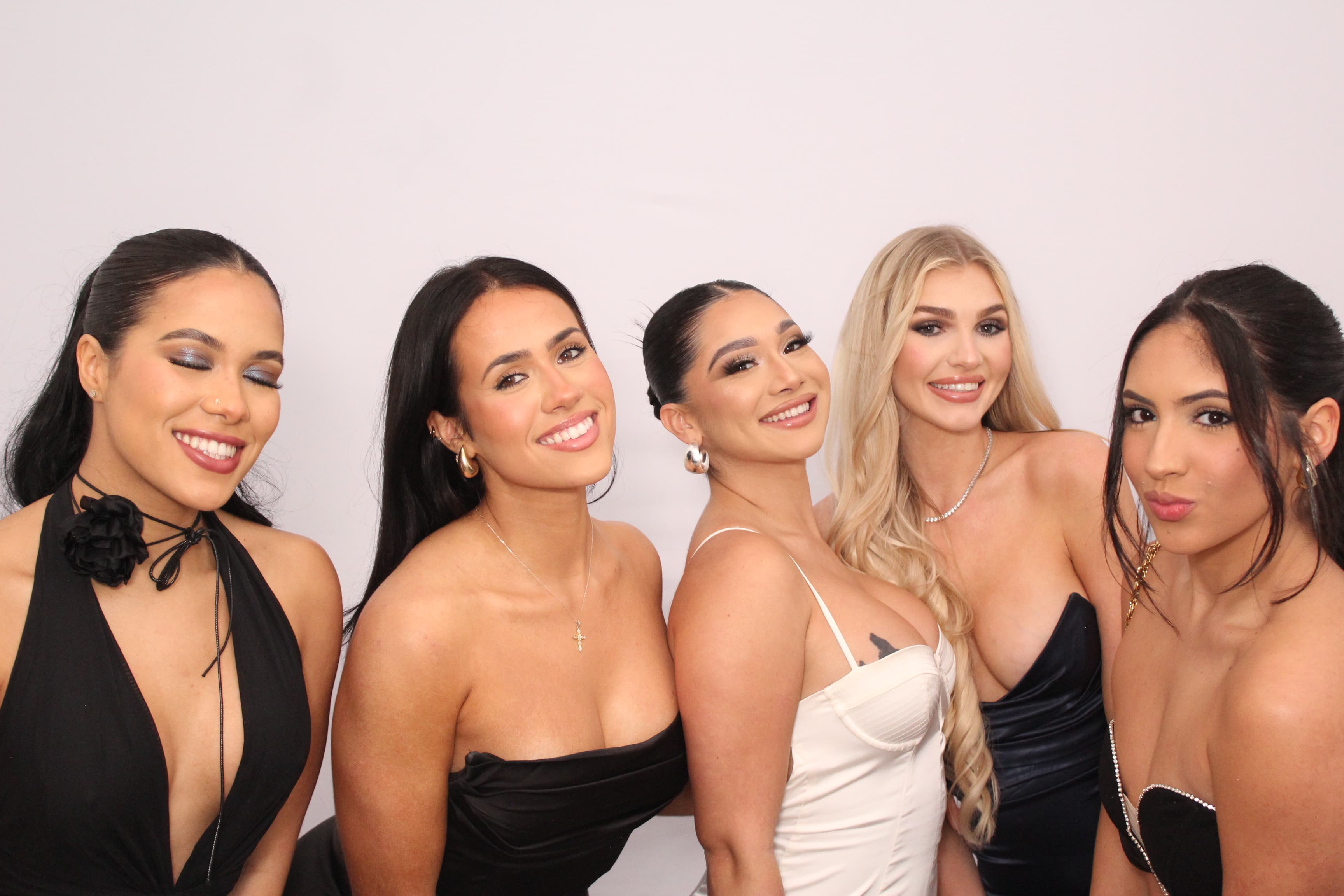 Five friends in black and ivory dresses smiling together in front of a plain white backdrop.