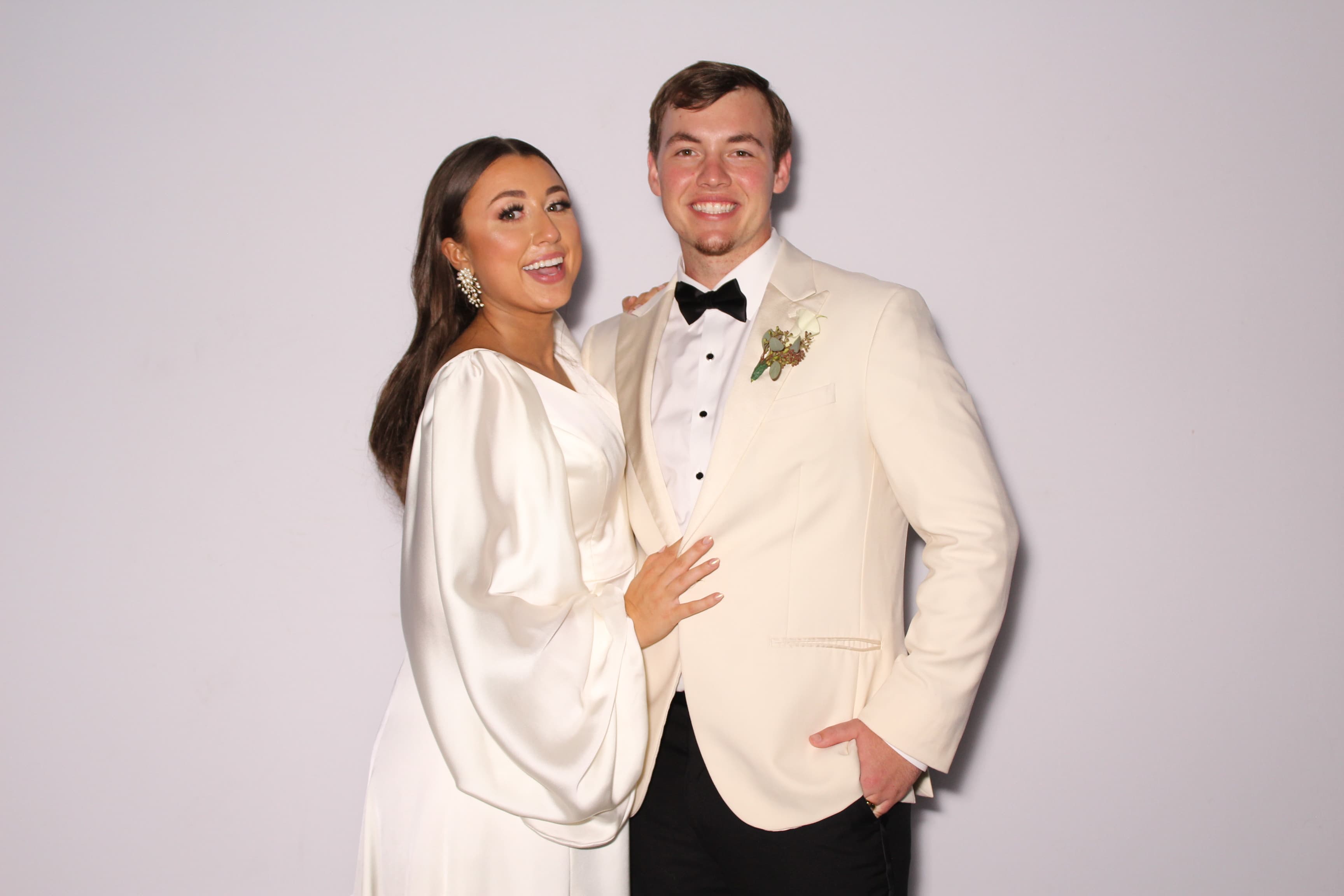 A bride in a flowing ivory gown and groom in a cream dinner jacket smiling together at their wedding.