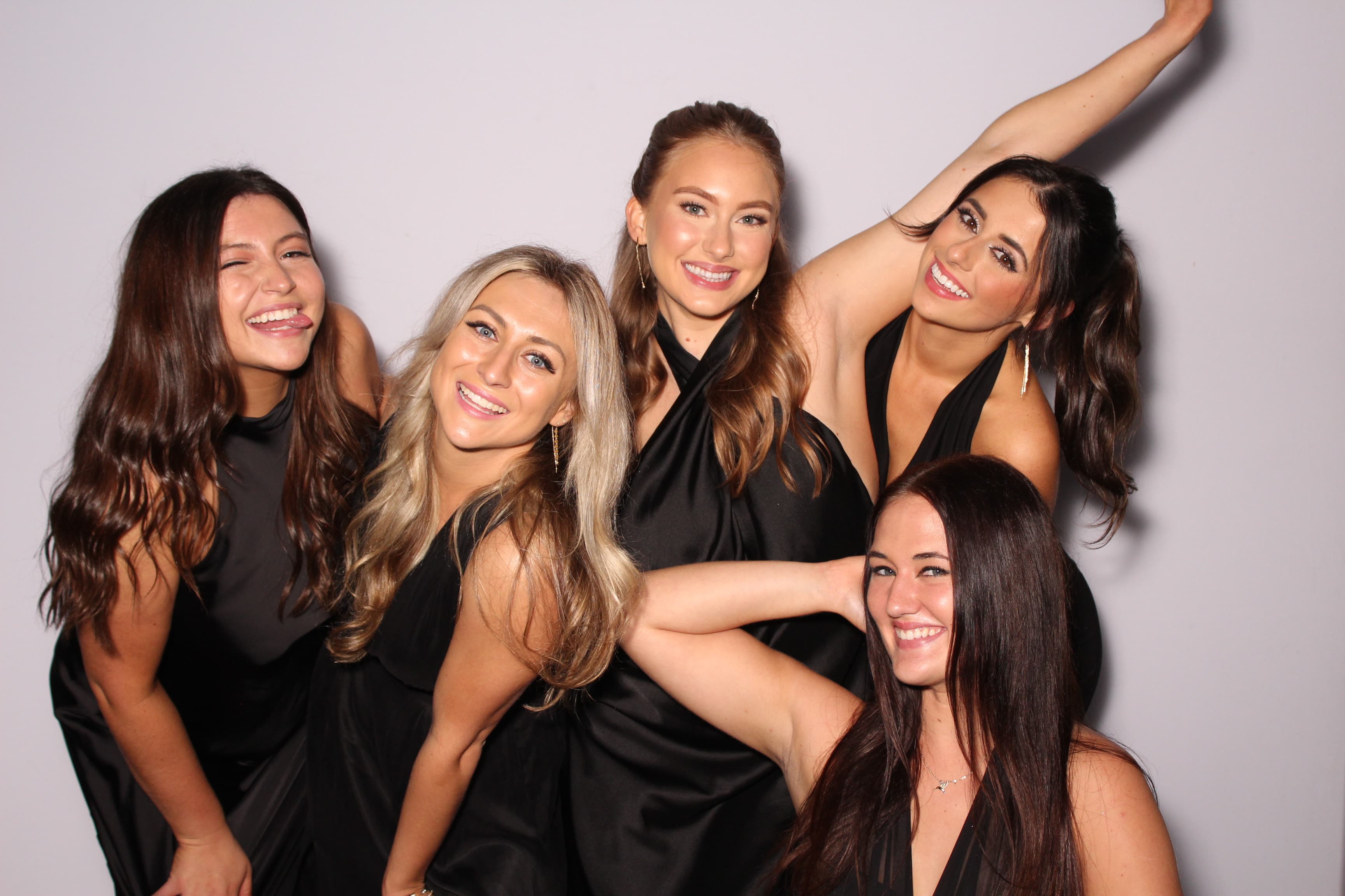 Five friends in black dresses laughing together in a playful group pose.