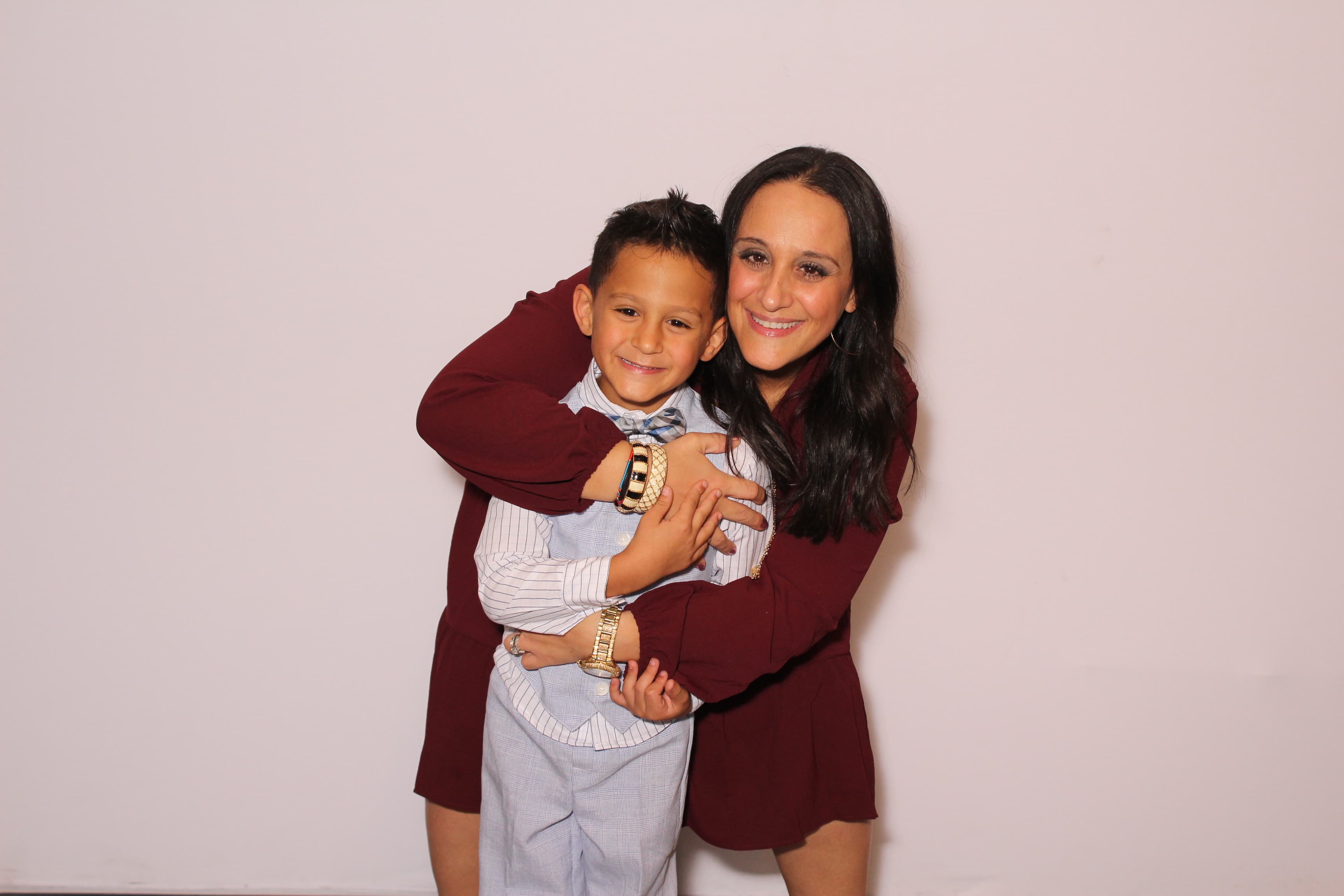 A mother warmly hugging her young son, both dressed up for a celebration.