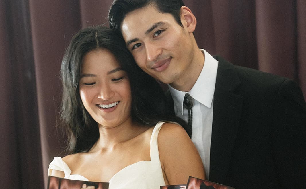 A couple in black tie holding their photo strips in front of a rich burgundy backdrop.