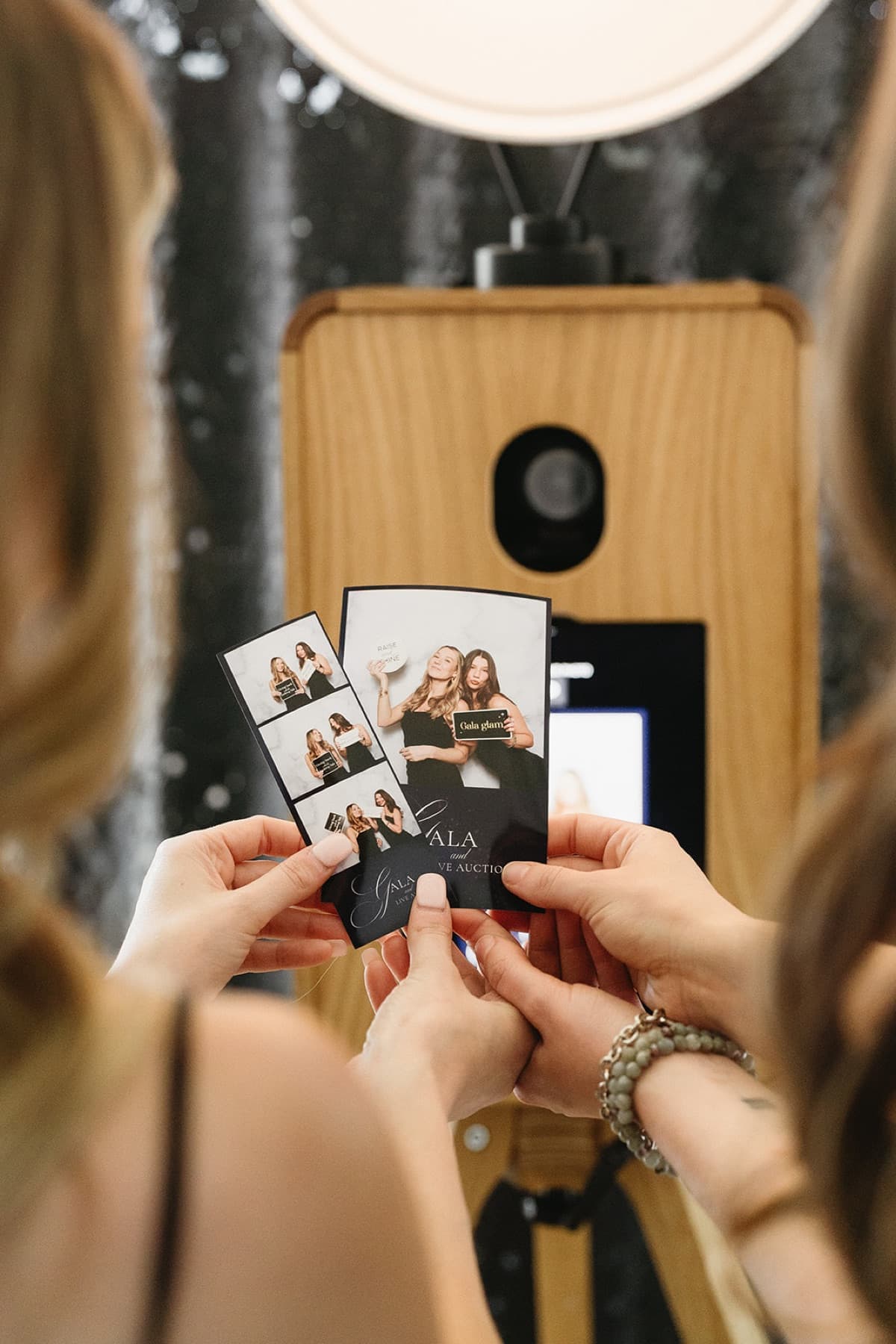 A guest holding a printed photo strip and portrait print in front of the MEMORI booth at a gala.