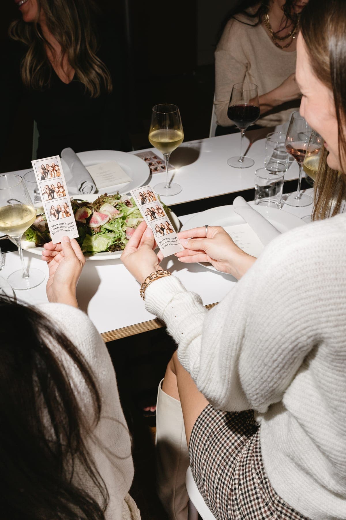 Two friends comparing their photo strips at a candlelit dinner table.